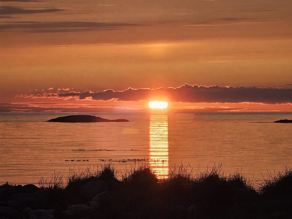 Midnattssol over havet med refleksjon i vannet